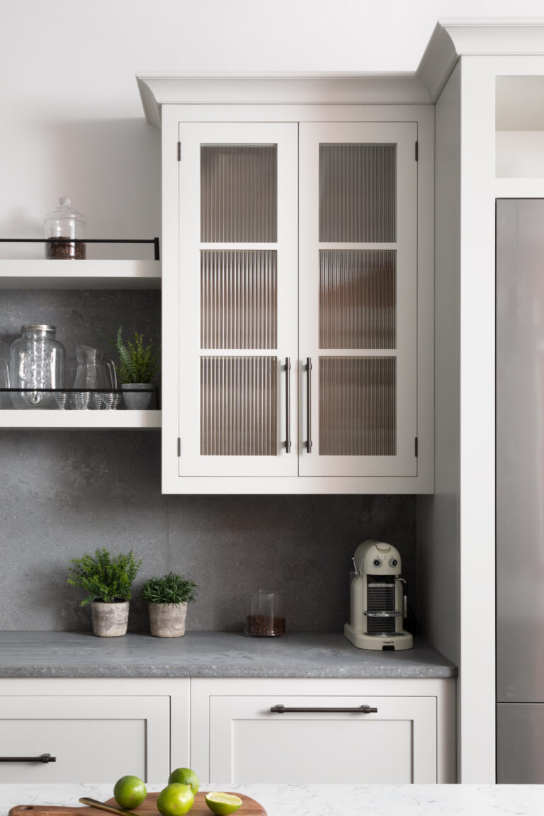 Kitchen wall cabinet with fluted glass doors and bronze handles, above a dark stone worktop with open shelving
