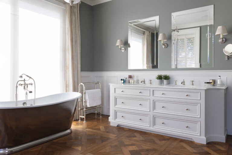 Luxury master bathroom with freestanding roll-top bath, white double vanity unit and parquet flooring
