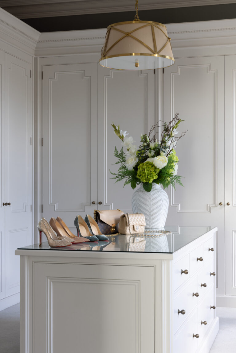 Dressing room island with panelled wardrobes, drawers and a pendant light, displaying shoes, handbags and a floral vase