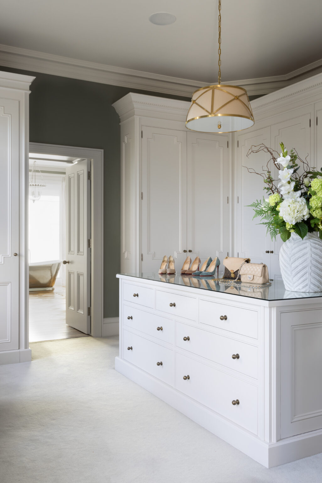 Dressing room with bespoke white cabinetry and central island of drawers displaying shoes and handbags
