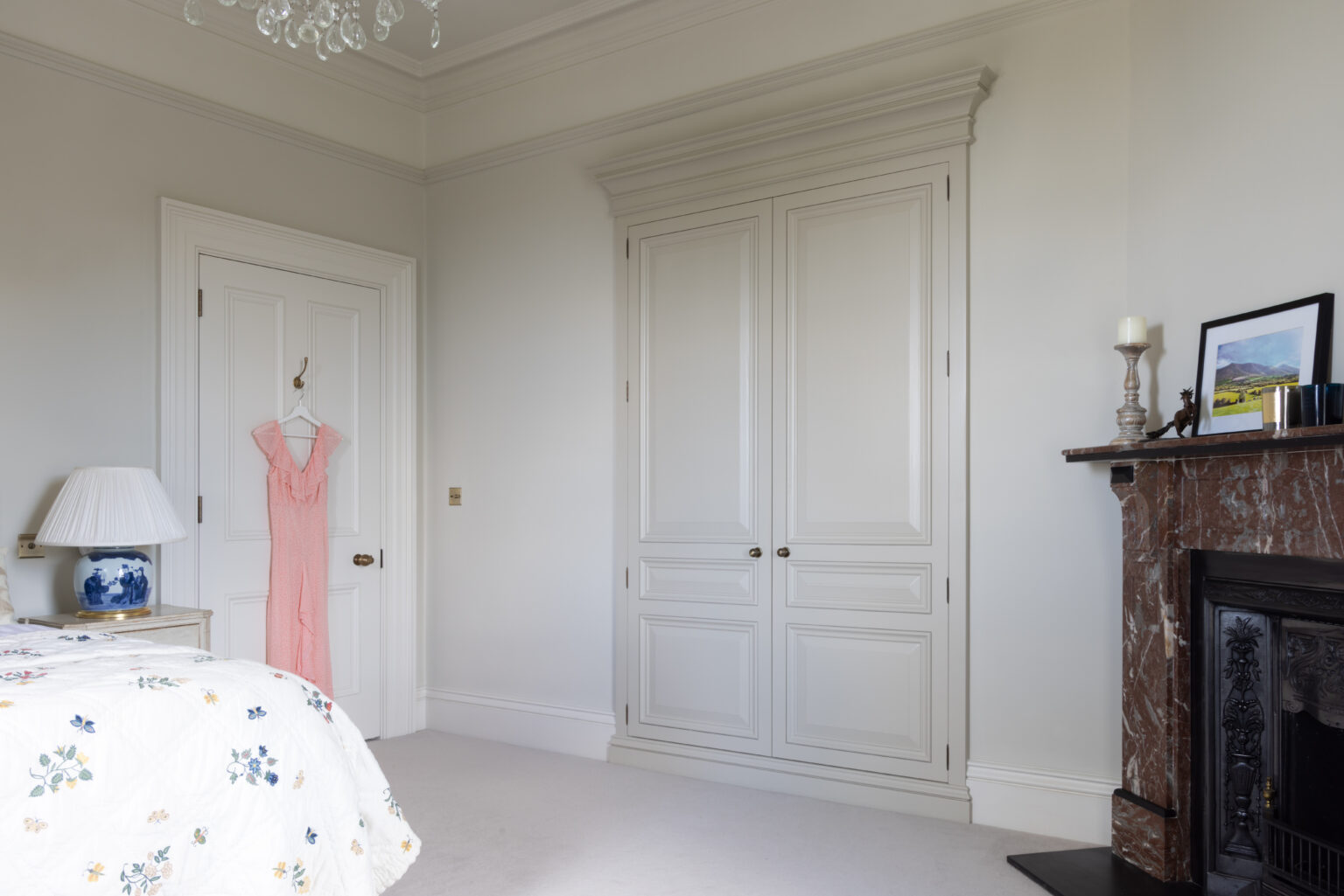 Bedroom with a fitted panelled wardrobe, period fireplace and cornicing, alongside a bed and bedside lamp