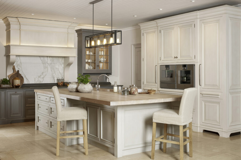 Kitchen with a large timber-topped island, bar stools, panelled cabinetry and integrated ovens beneath a glass-fronted display cupboard