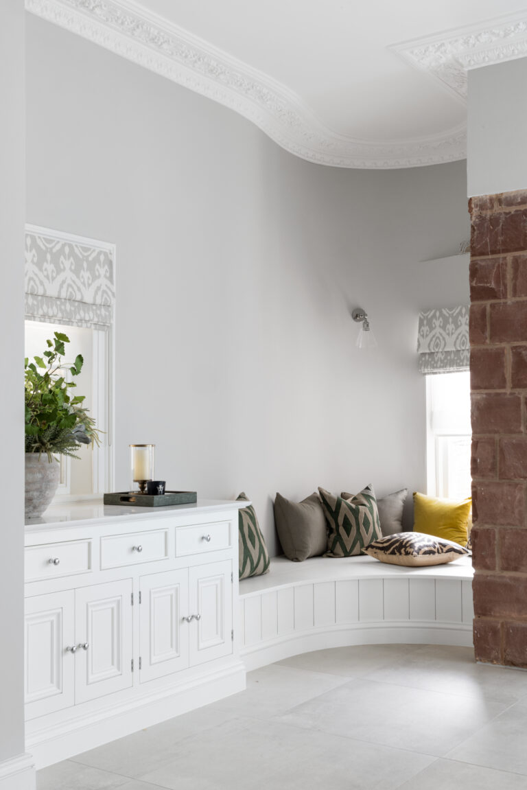 Curved reading nook with scatter cushions beside white cabinetry and an exposed sandstone wall near the window