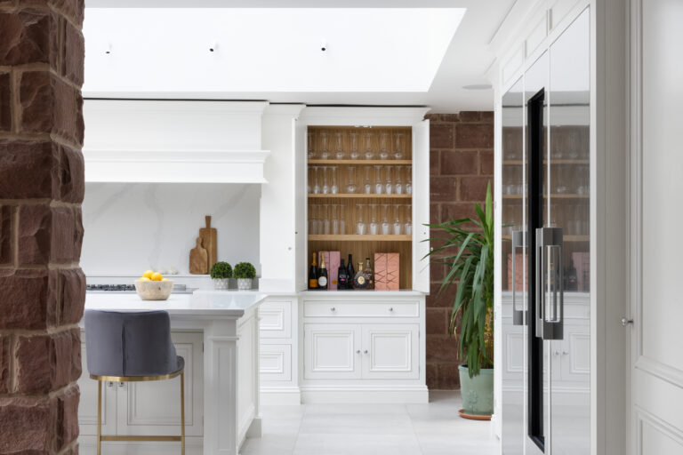 White kitchen cabinetry framed by an exposed sandstone wall, with an open drinks cupboard revealing glassware and bottles