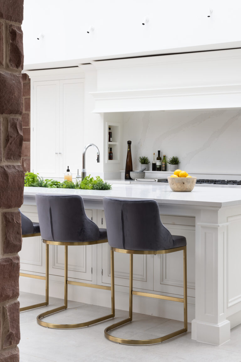 White painted kitchen island with velvet bar stools, set beside an exposed sandstone wall pillar