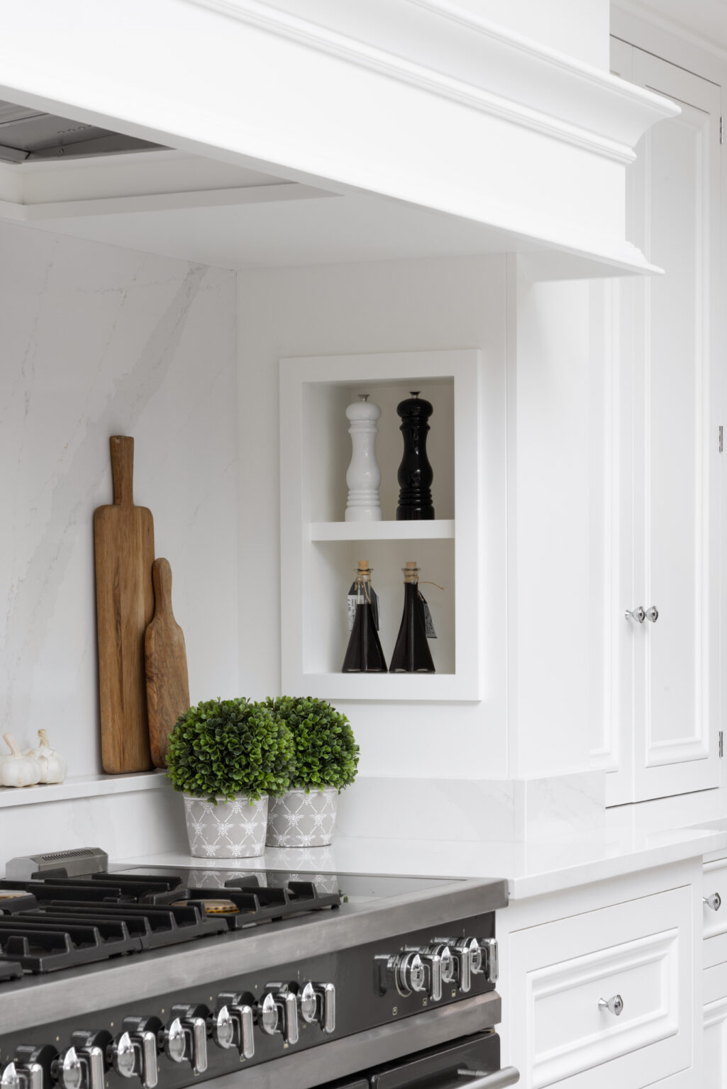 White kitchen cabinetry with a built-in wall niche, extractor hood and freestanding range cooker beneath