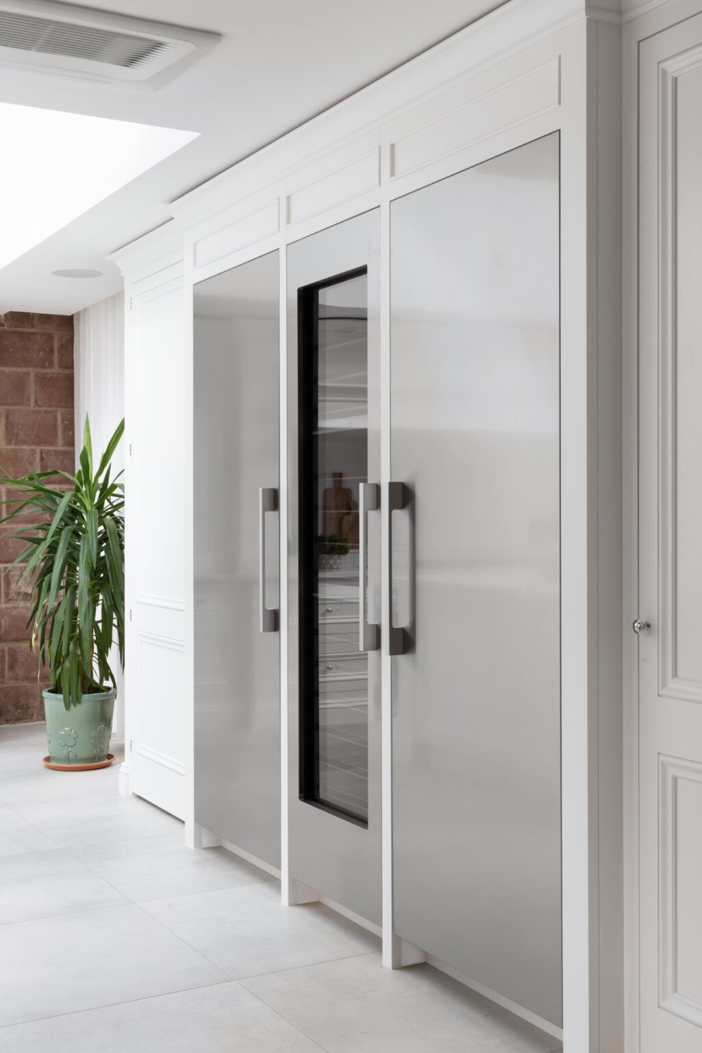 White kitchen cabinetry houses integrated fridge and wine cooler, with exposed sandstone wall visible through the doorway