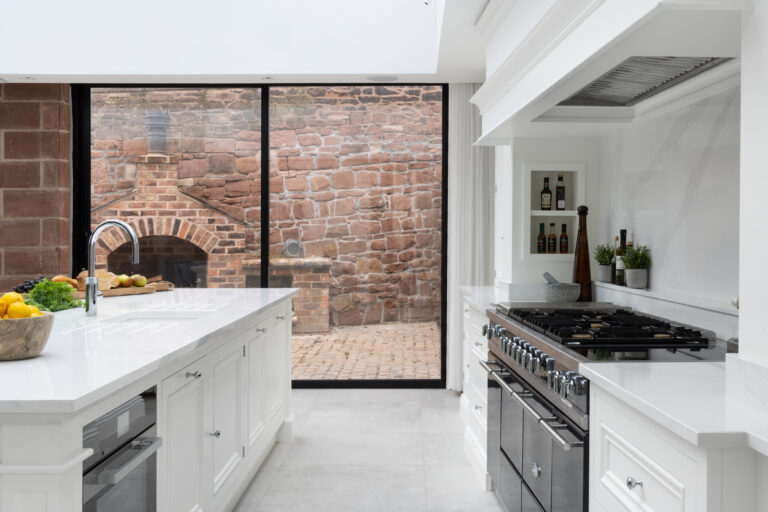 White kitchen with island, range cooker and glazed doors framing the exposed sandstone wall outside