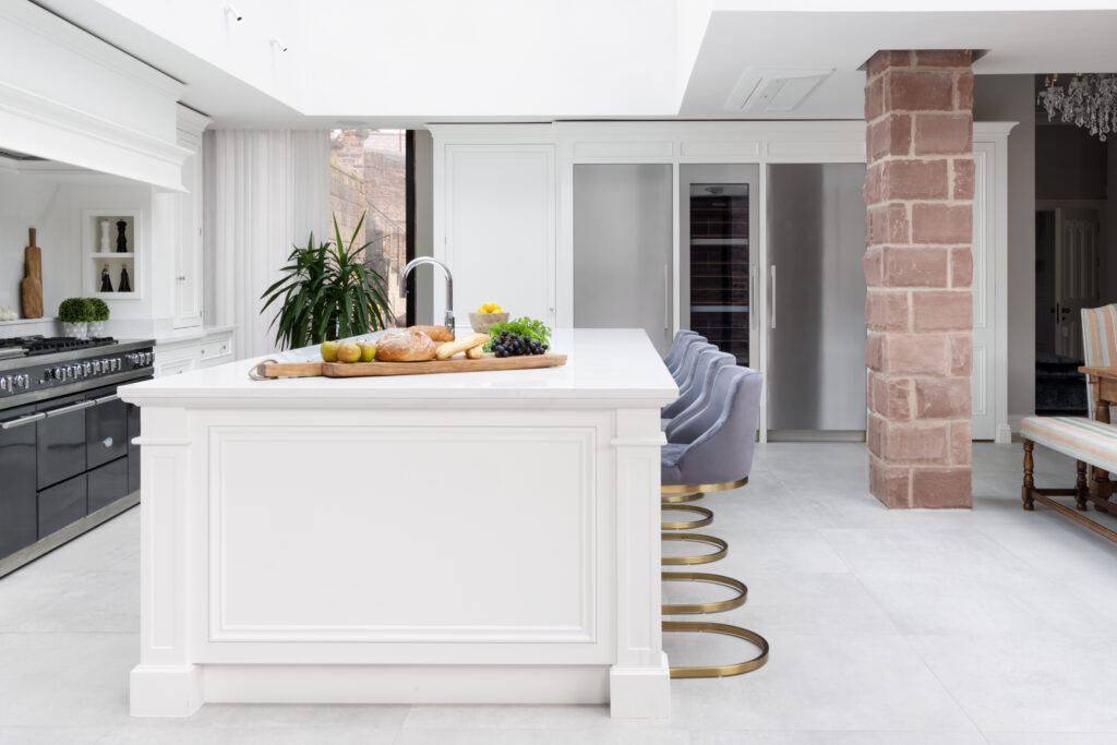 White kitchen island with velvet bar stools, set against an exposed sandstone wall and range cooker