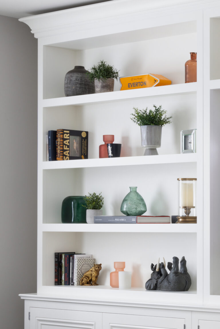 White bespoke shelving unit displaying books, vases, plants and ornaments across four open shelves