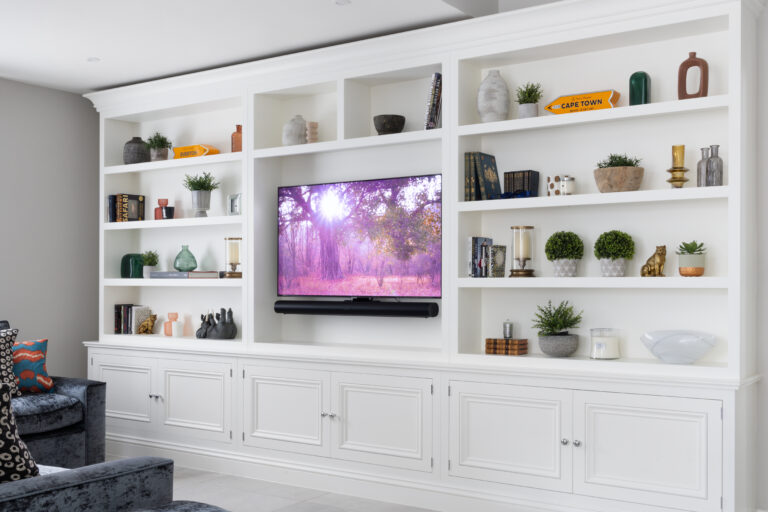 Built-in white media lounge shelving with cupboards below and a wall-mounted television flanked by open display shelves