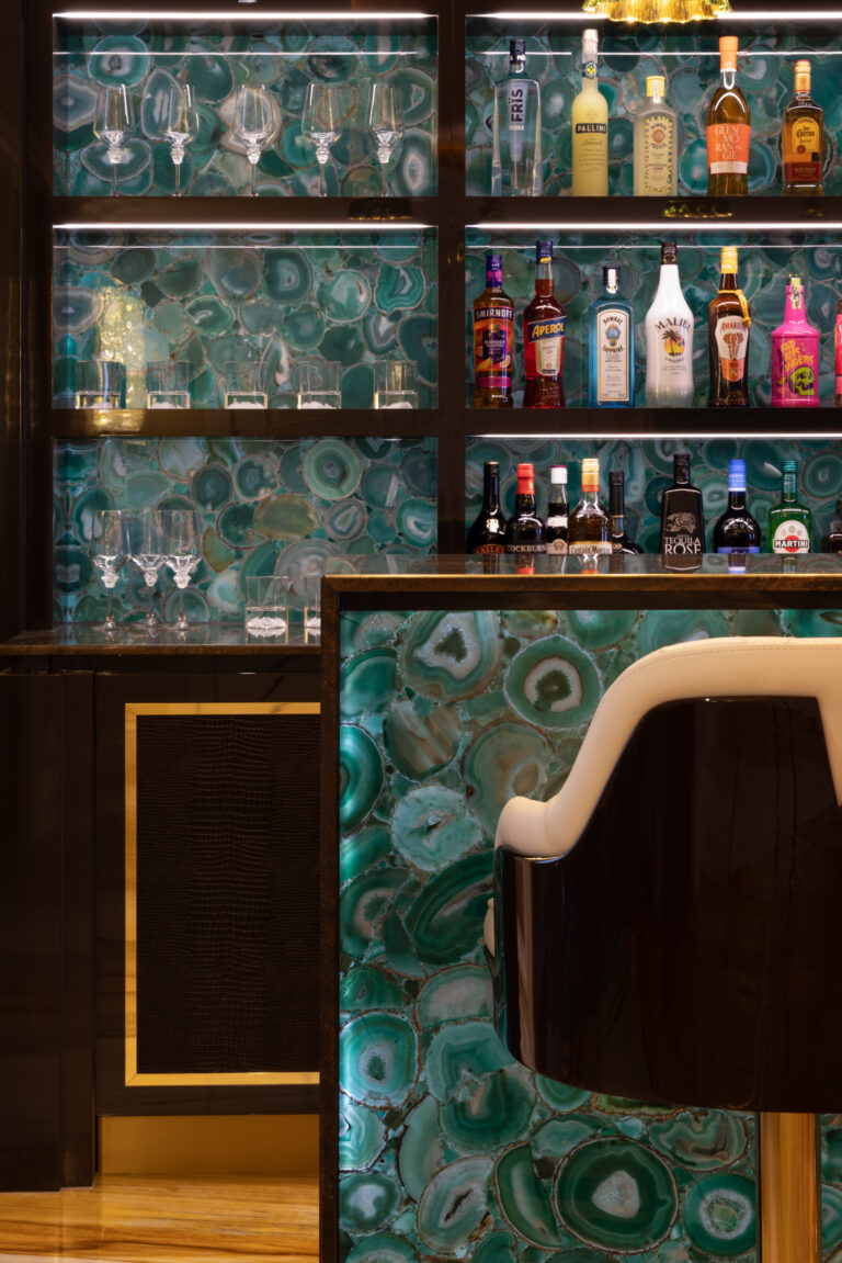 Backlit green agate bar with gold-edged shelving, glassware and spirit bottles above a cream leather stool