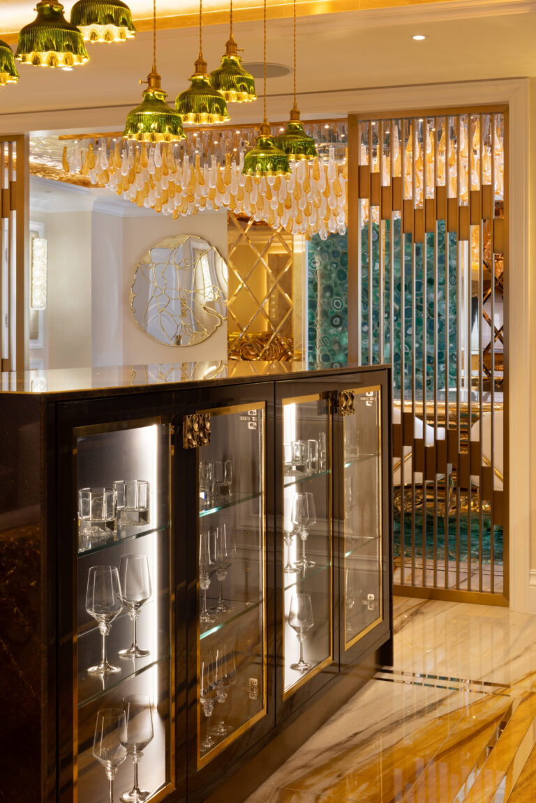 Bar area with glass-fronted cabinetry, gold pendant lighting and a green agate feature wall behind brass fins