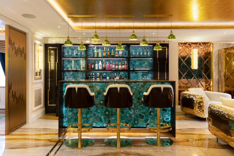 Backlit green agate bar with gold-finished stools, pendant lights and shelving holding glassware and bottles