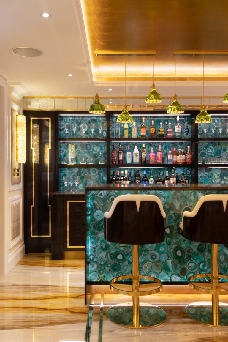 A green agate bar with backlit shelving, gold pendant lights and gold-trimmed bar stools with glossy black backs
