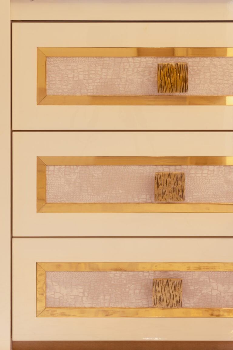 Close-up of dressing room drawers with textured inset panels, gold trim edging and square gold knobs