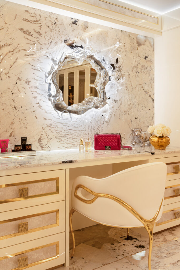 Dressing table with gold-trimmed drawers, sculpted mirror, and a gold-framed chair beneath a stone splashback