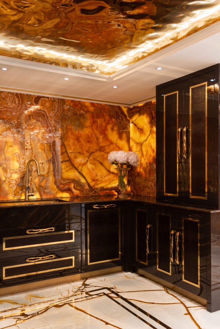 Backlit onyx walls and ceiling glow above black cabinetry with gold-edged handles and a sculptural tap