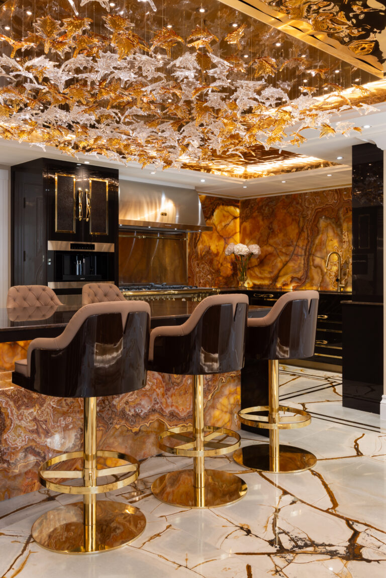 Kitchen island with backlit onyx cladding, gold-based bar stools and an ornate glass leaf ceiling fitting