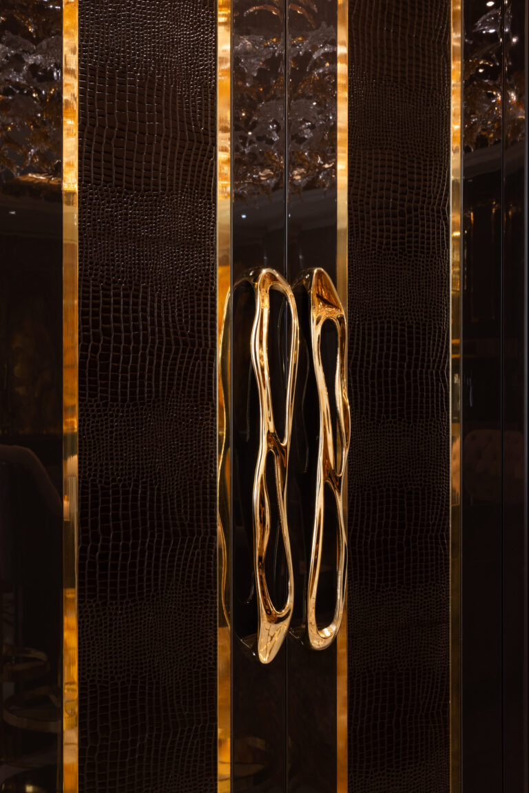 Close-up of cabinet doors with textured dark panels, gold trim strips and sculptural gold drip-style handles