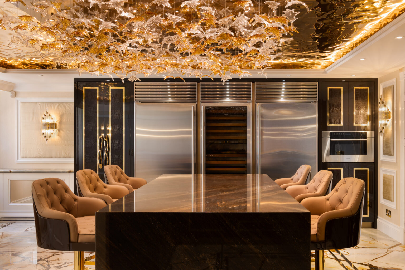 Kitchen island with tan leather stools beneath an ornate gold sculptural ceiling light, flanked by steel cabinetry