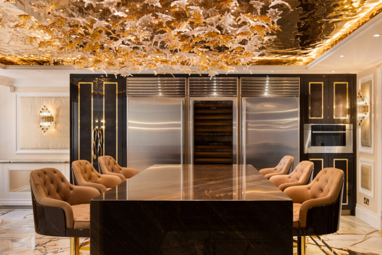 Kitchen island with tan leather stools beneath an ornate gold sculptural ceiling light, flanked by steel cabinetry