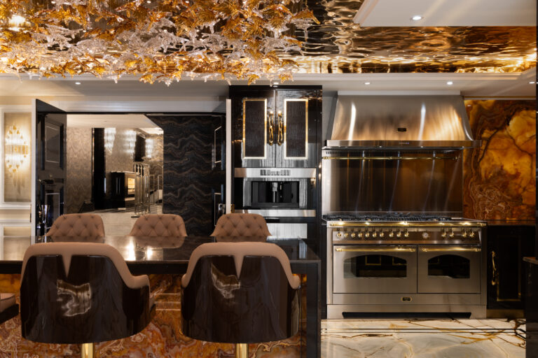 Kitchen island with backlit onyx surround, brass-trimmed range cooker and tufted bar stools beneath a sculptural chandelier