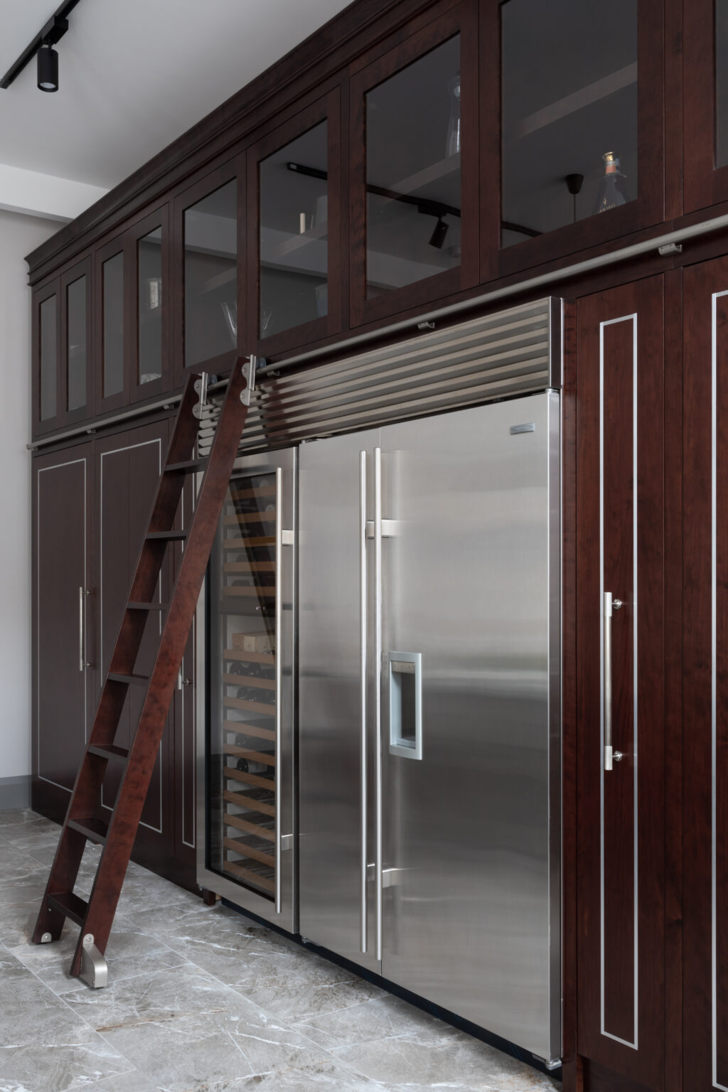 Tall deep-stained cherry wood cabinetry with sliding ladder, glass-fronted units and integrated stainless steel fridge and wine cooler