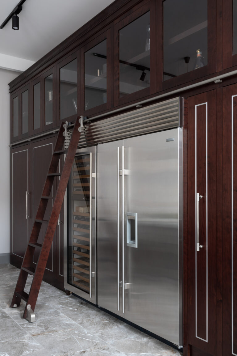 Tall deep-stained cherry wood cabinetry with sliding ladder, glass-fronted units and integrated stainless steel fridge and wine cooler