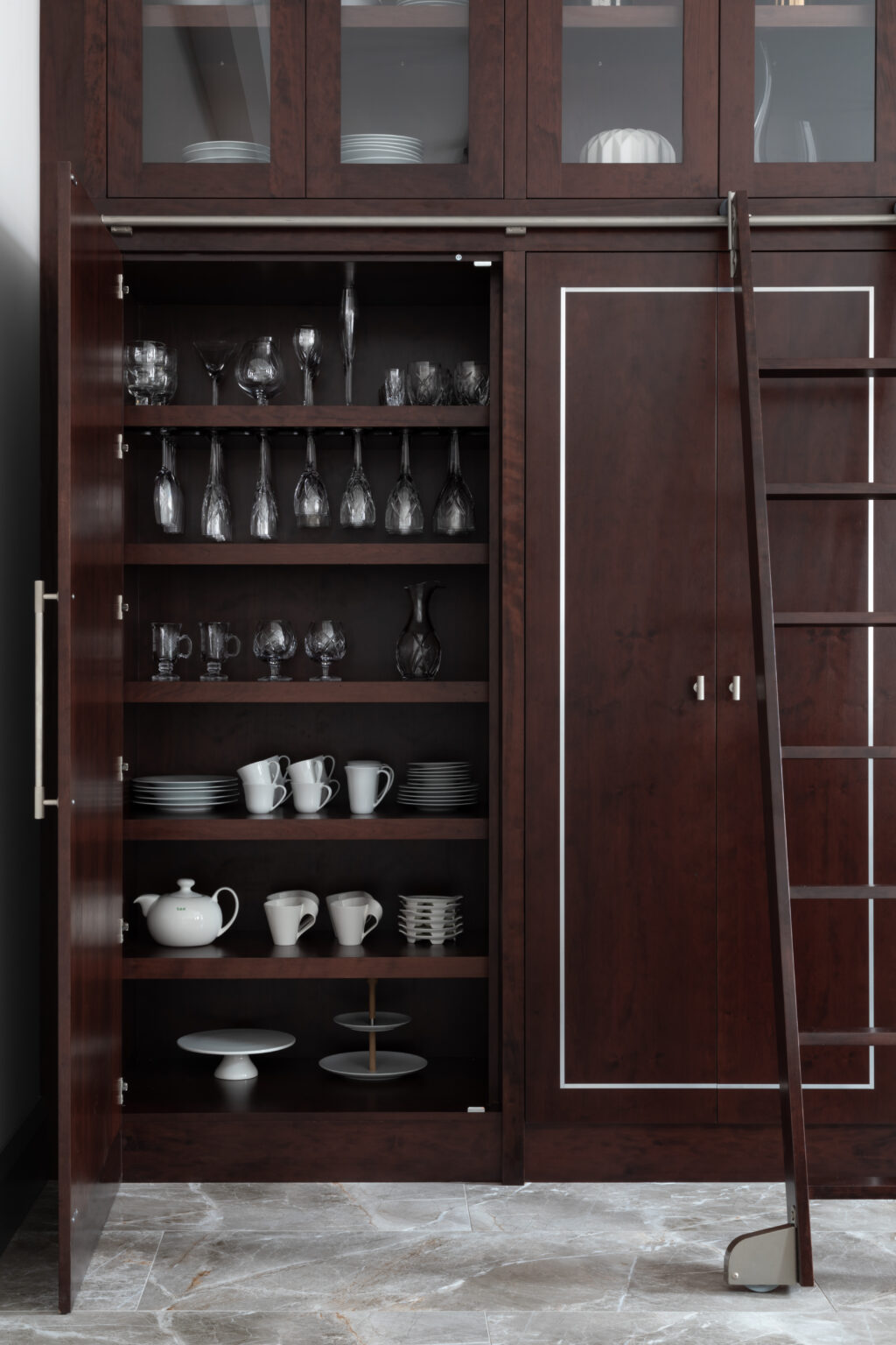 Deep-stained cherry wood cabinetry with open shelving for glassware and crockery, plus a sliding library ladder