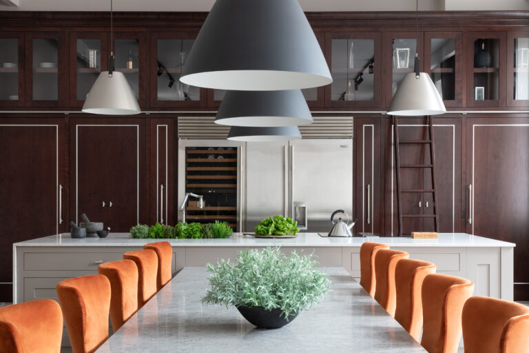 Kitchen island with orange upholstered chairs, large pendant lights, and cherry wood cabinetry with a library ladder
