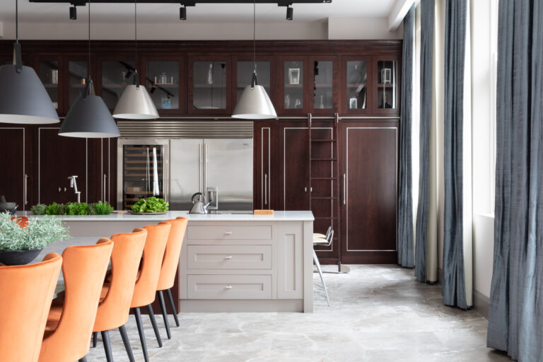 Kitchen island with orange velvet stools beneath the deep-stained cherry wood library wall and rolling ladder