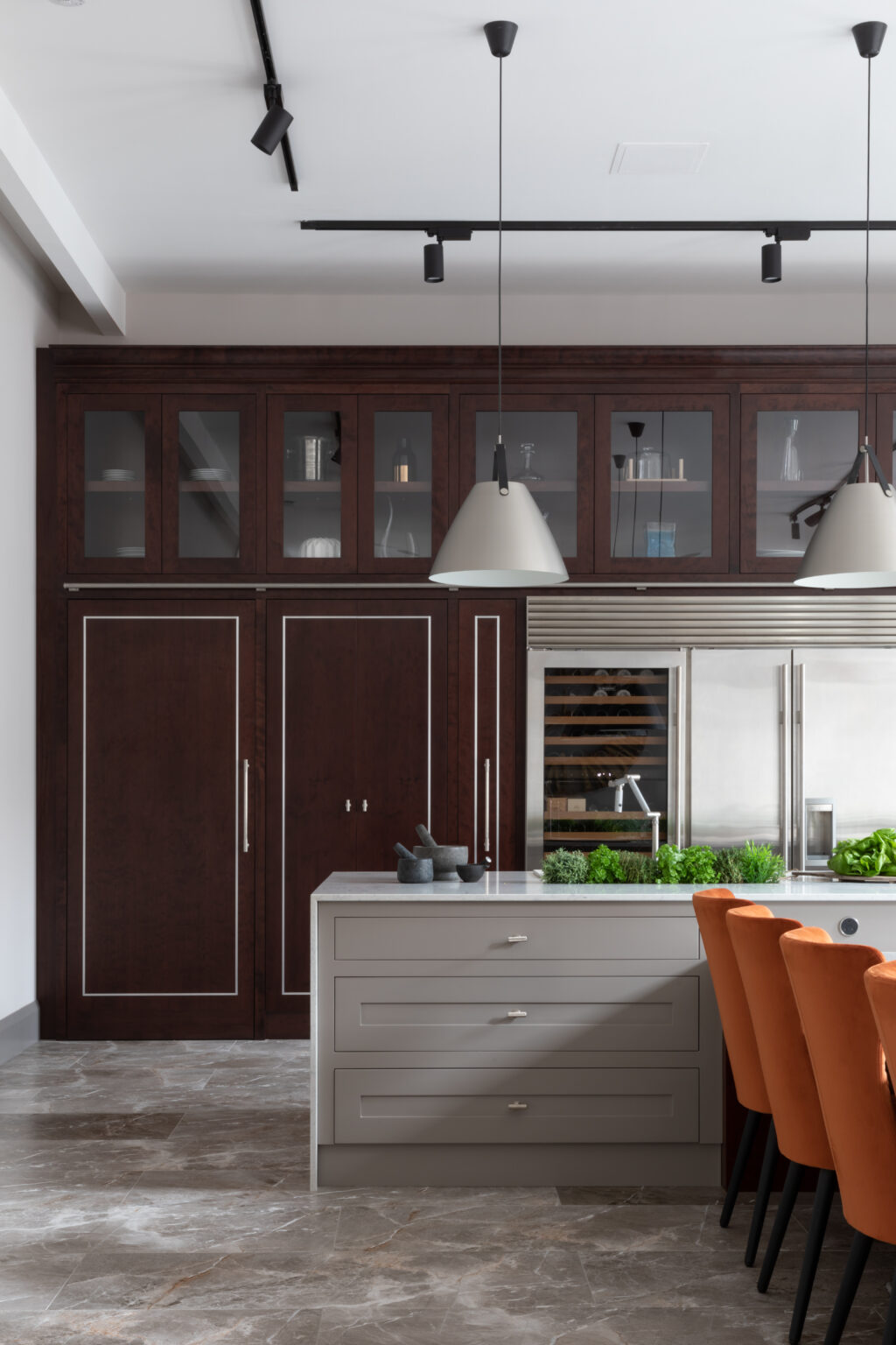 Kitchen with tall cherry wood cabinetry, integrated fridge, grey island and orange upholstered stools