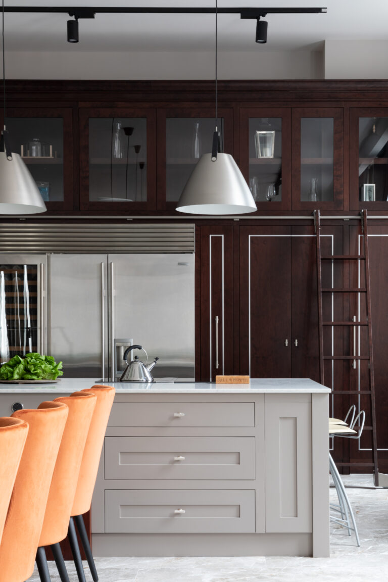 Kitchen island with pendant lights, orange stools and a ladder leading up to the deep-stained cherry wood library wall