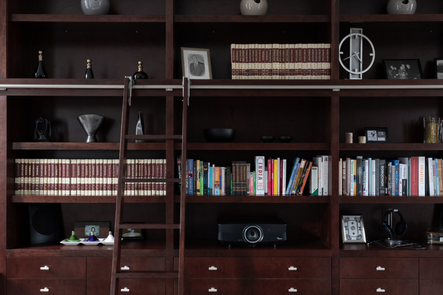 Deep-stained cherry wood library wall with sliding ladder, shelved books, drawers and decorative ornaments on display