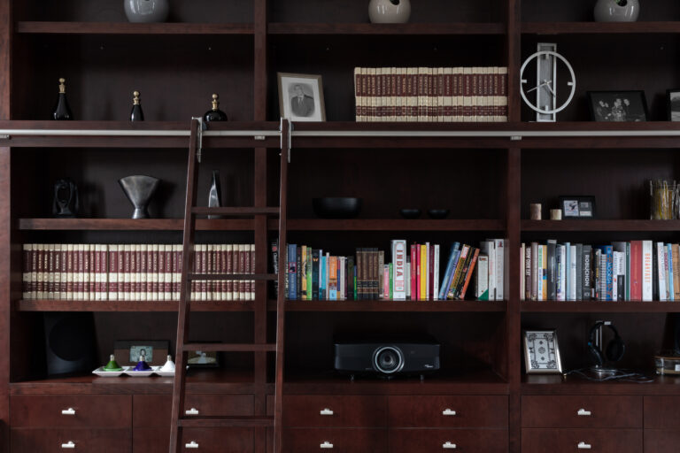 Deep-stained cherry wood library wall with sliding ladder, shelved books, drawers and decorative ornaments on display