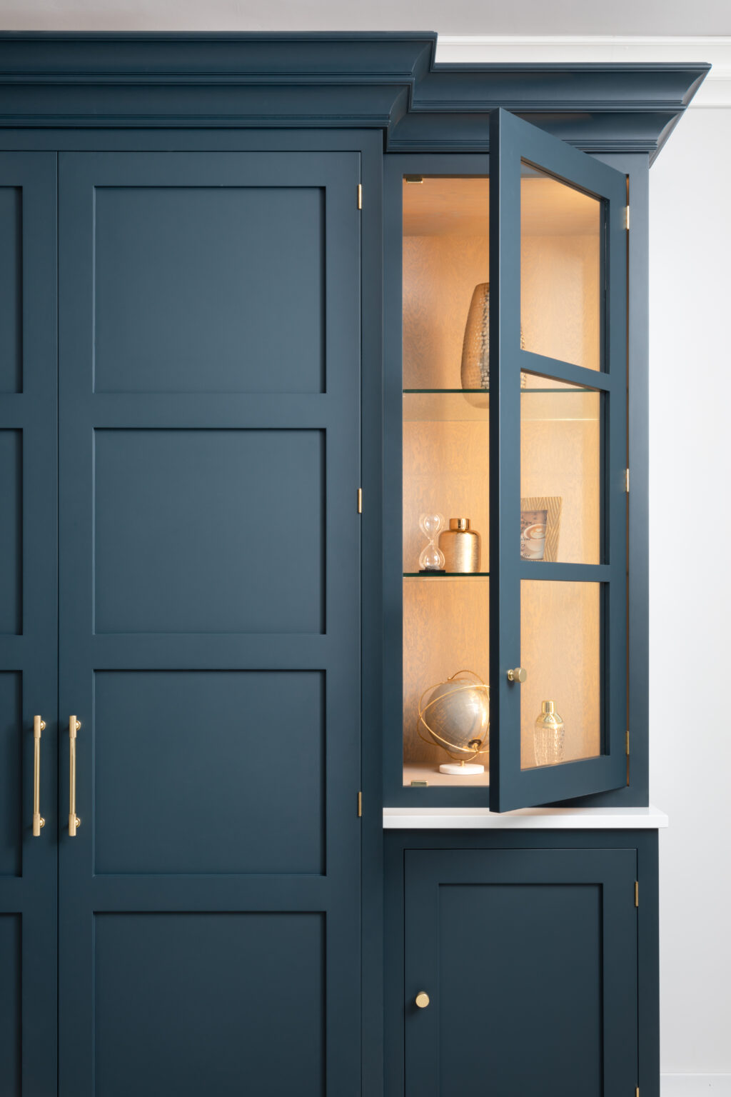Hague Blue cabinetry with a glazed display cabinet door open, showing lit shelves with decorative ornaments and brass hardware