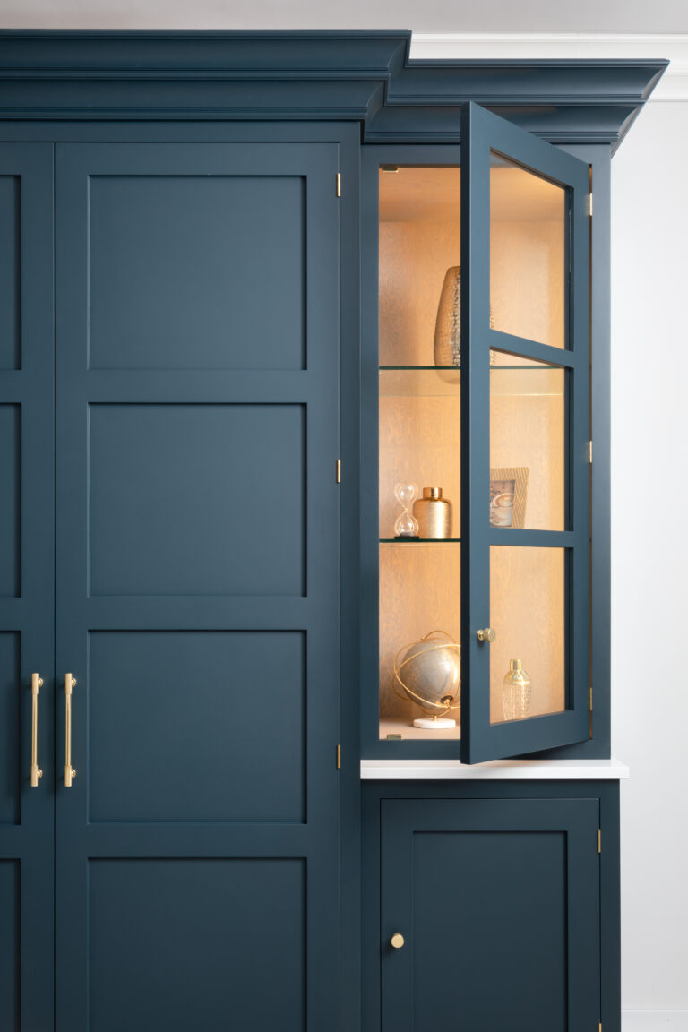Hague Blue cabinetry with a glazed display cabinet door open, showing lit shelves with decorative ornaments and brass hardware