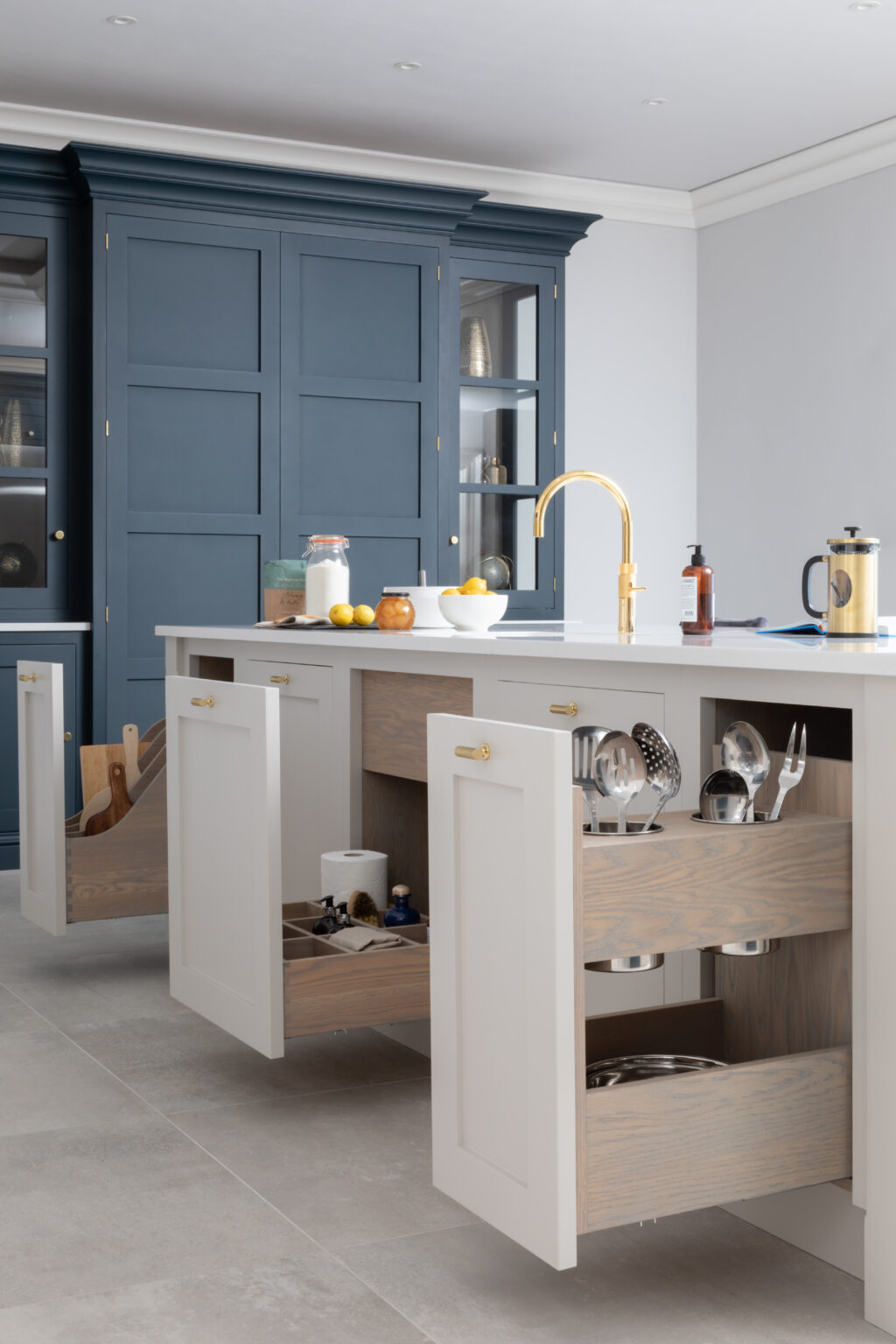 Cornforth White island with open drawers showing utensil storage, beside a Hague Blue dresser and gold tap