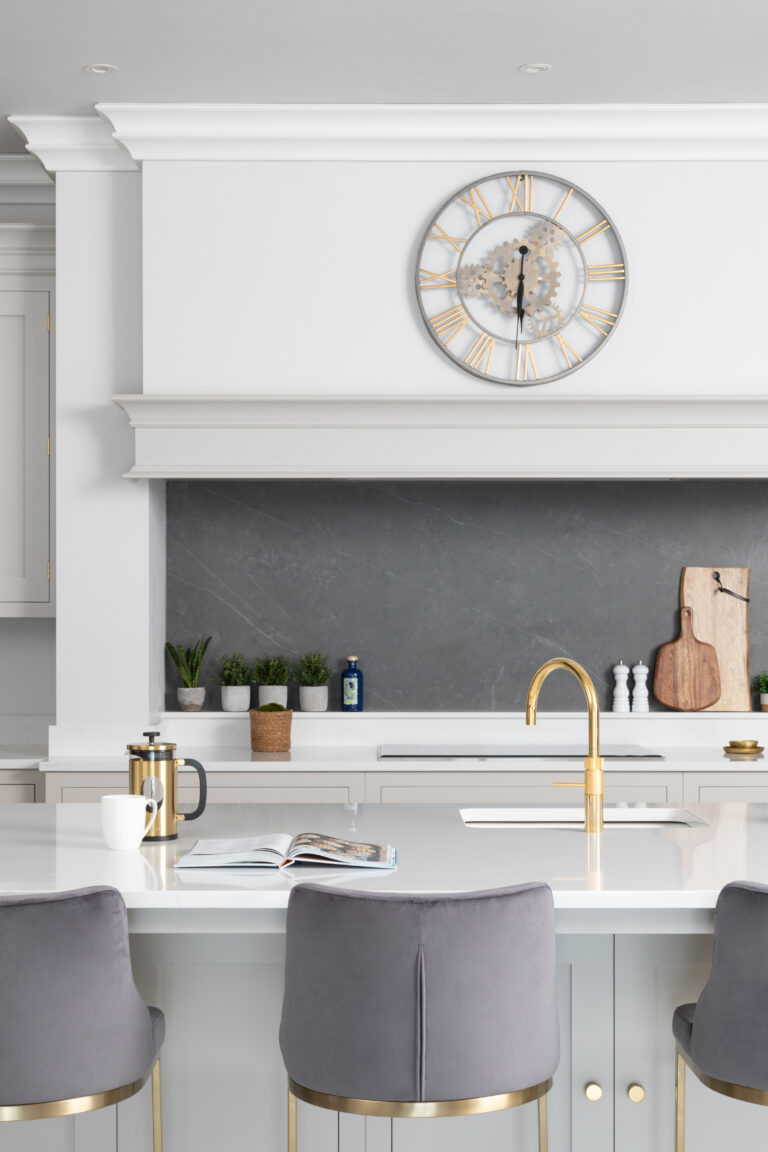 Island with grey velvet bar stools and a gold Quooker tap, set before Cornforth White cabinetry and a dark stone splashback