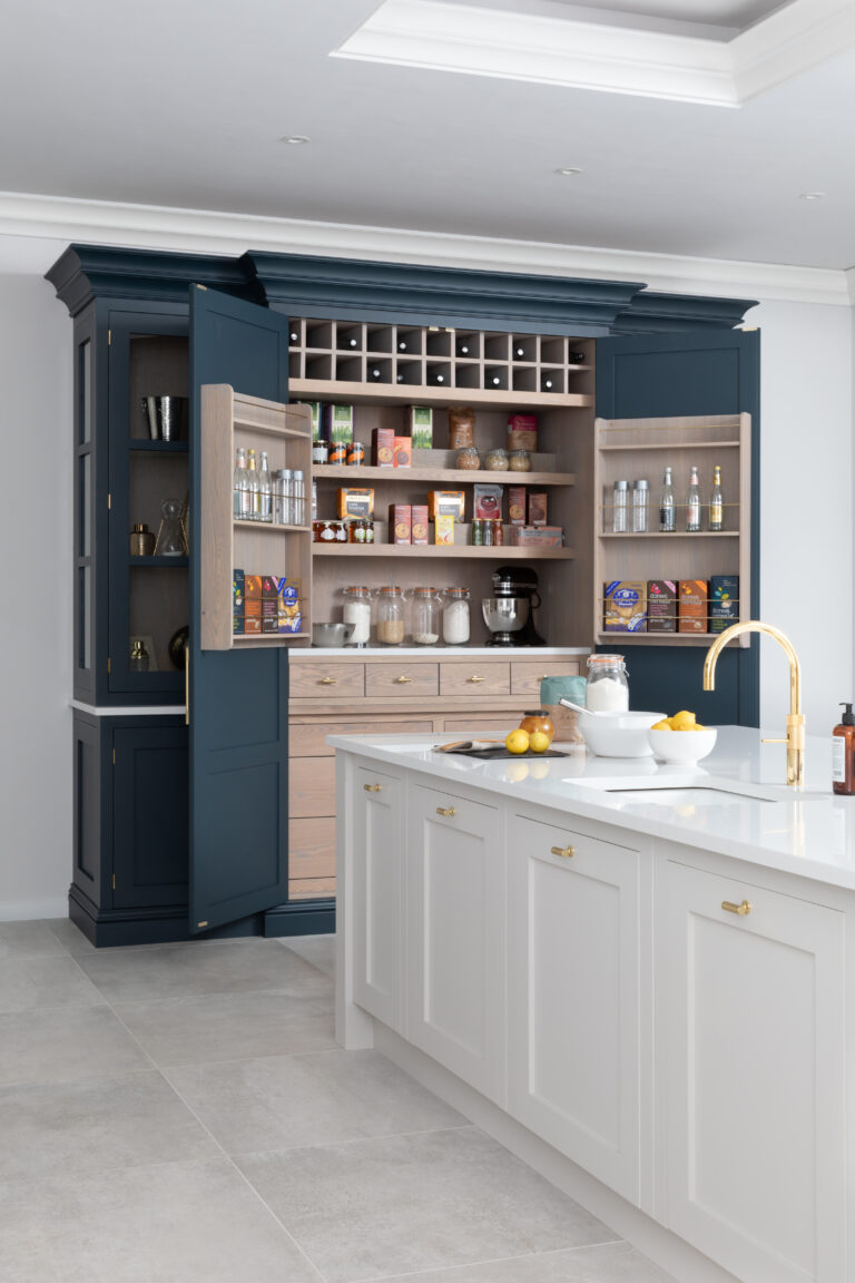 Large Hague Blue pantry cupboard stands open beside the island, revealing wine racking, shelving and stocked drawers