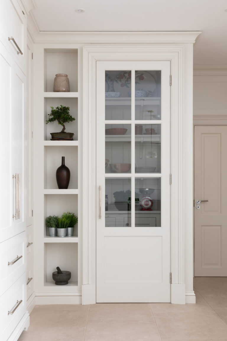Glazed pantry door with panelled frame beside open display shelving holding crockery and small plants