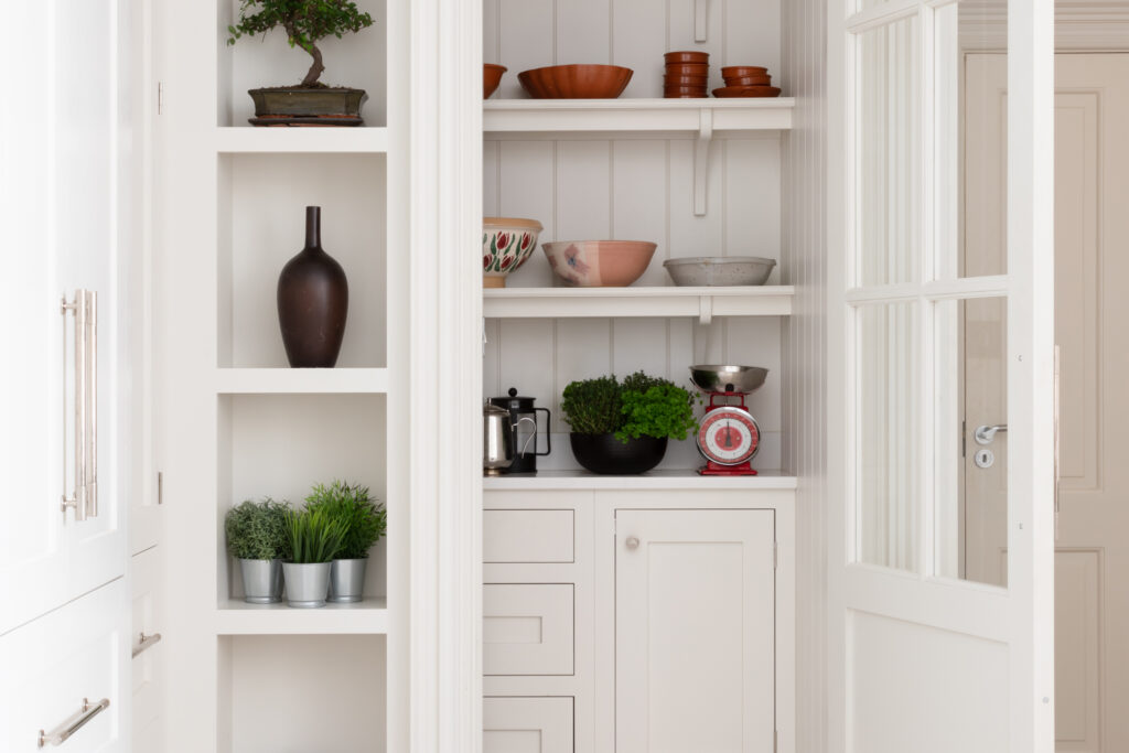 Walk-in pantry with tongue-and-groove panelling, open shelves on curved corbels, and cabinetry holding bowls and herbs