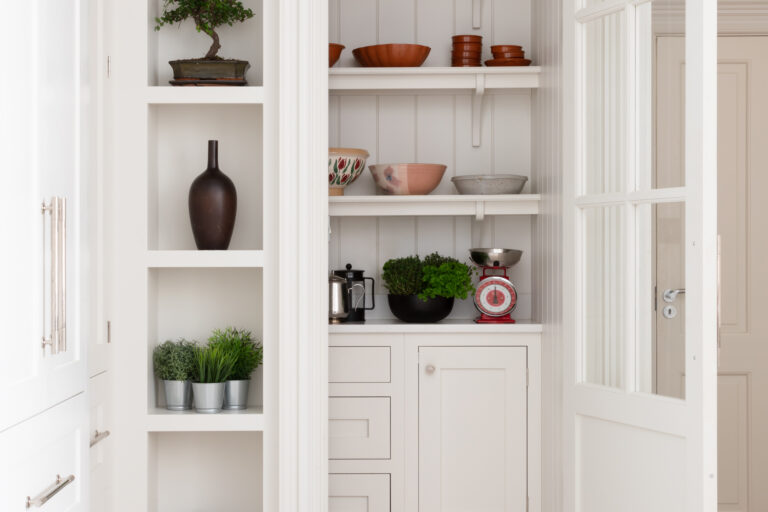 Walk-in pantry with tongue-and-groove panelling, open shelves on curved corbels, and cabinetry holding bowls and herbs