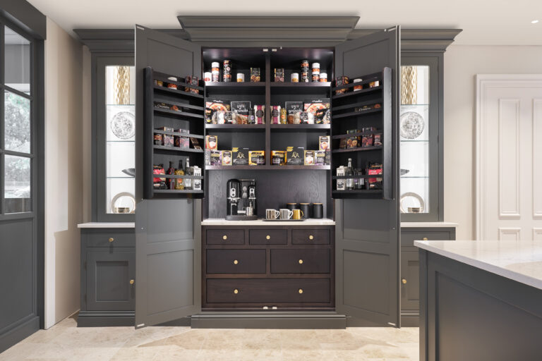 Hidden pantry cupboard with open doors revealing stocked shelves, drawers and a built-in coffee station with brass handles