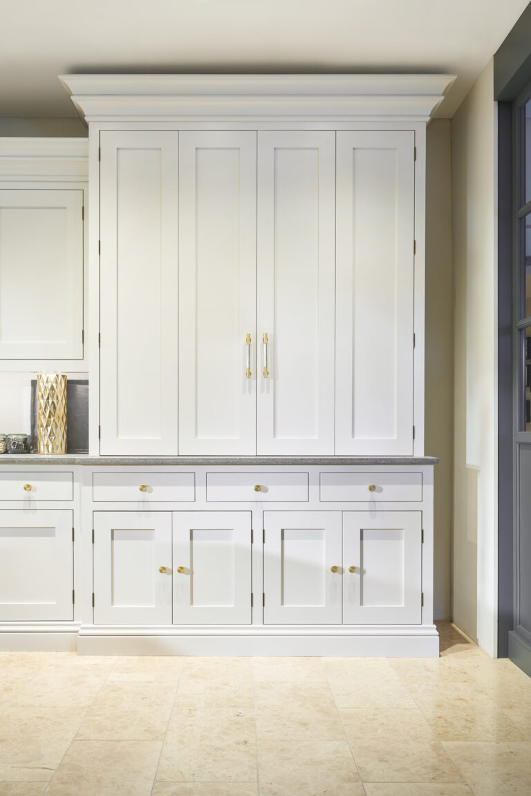 Tall painted pantry cupboard with panelled doors, drawers and polished brass handles, set against a pale wall