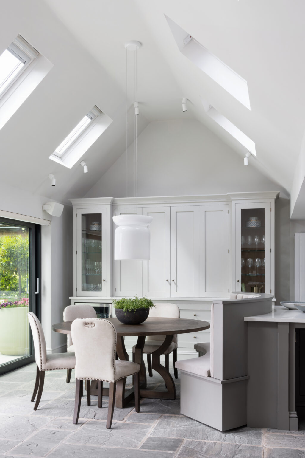 Vaulted ceiling dining area with round table, upholstered chairs, built-in dresser and curved banquette seat beside the island