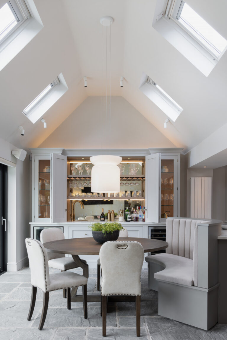 Vaulted dining area with round table, upholstered chairs and banquette seat facing a bespoke home bar