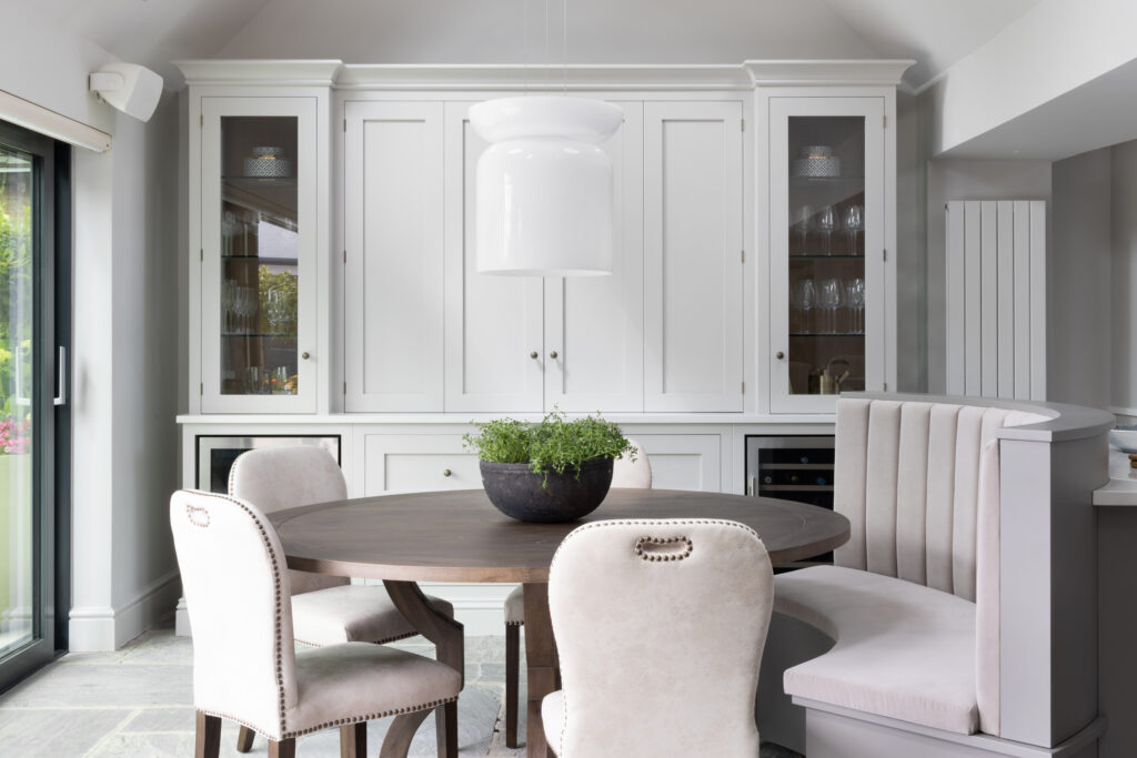 Round dining table with upholstered chairs beside the curved banquette seat and painted glazed display cabinetry