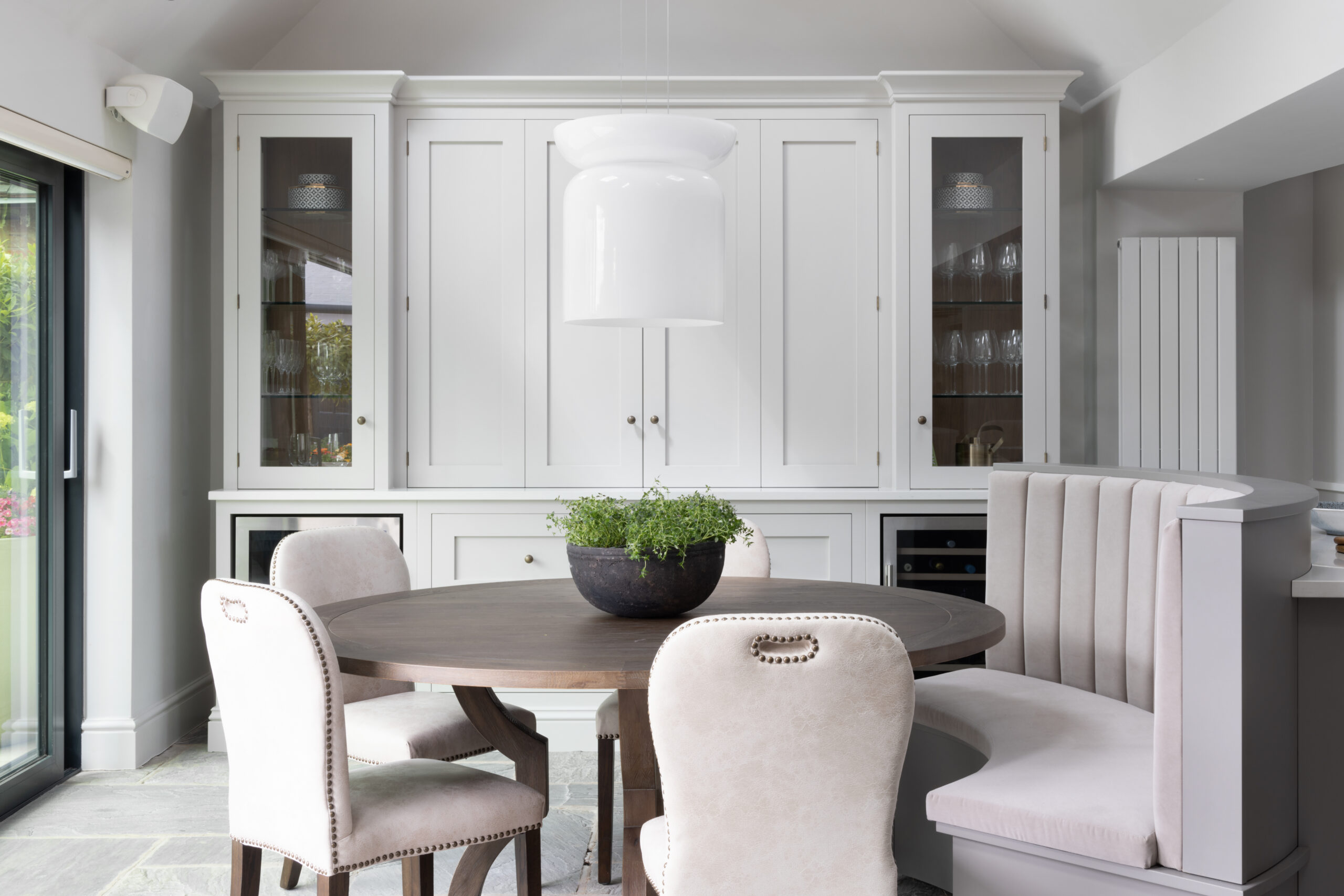 Round dining table with upholstered chairs beside the curved banquette seat and painted glazed display cabinetry